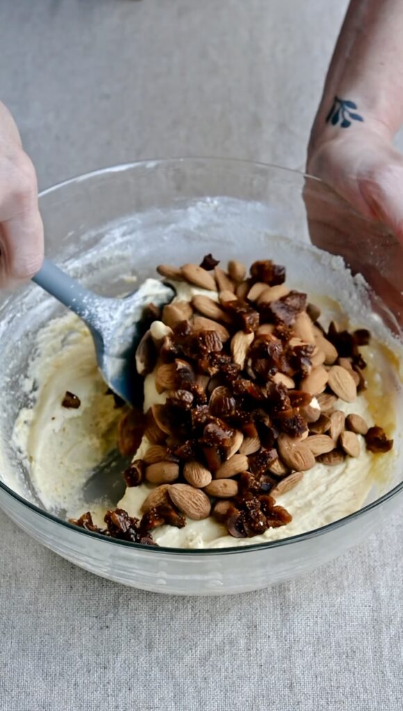 A silicone spatula folding almonds and figs into biscotti dough.
