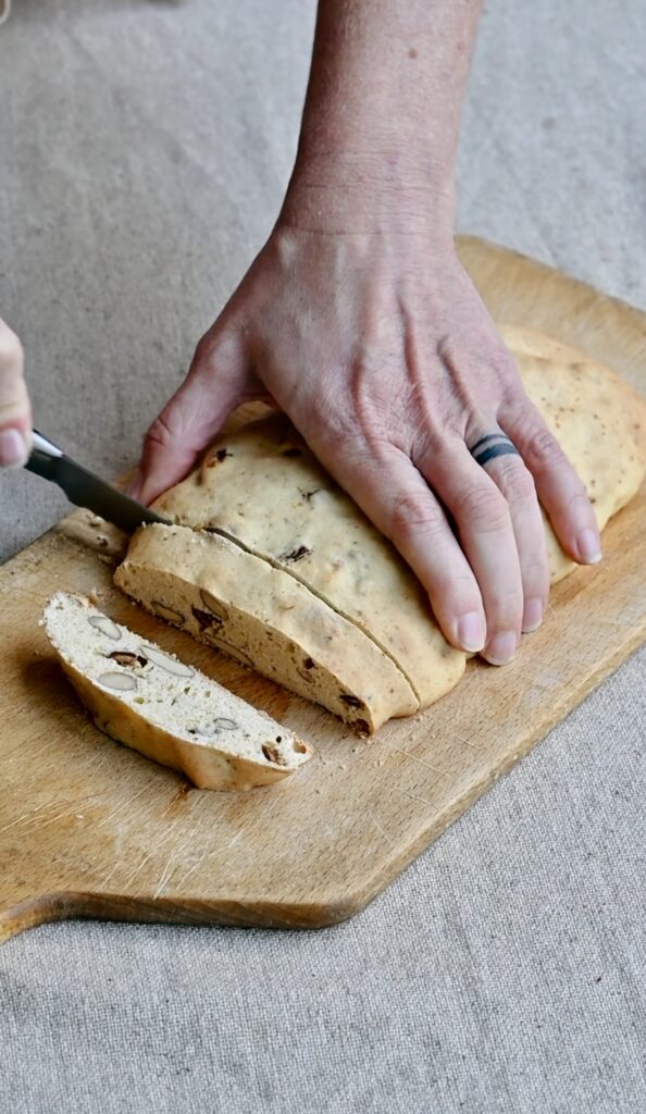 A baked biscotti log being cut into slices on a cutting board.