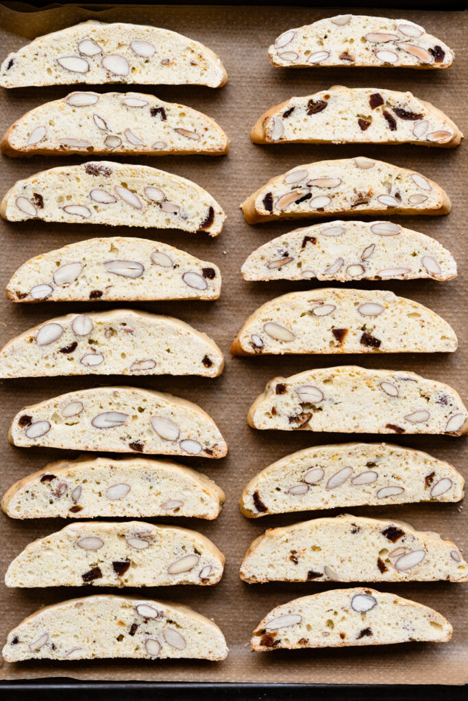Overhead of sliced almond biscotti cookies in two rows on a baking sheet.