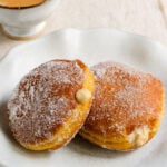 Two pumpkin donuts filled with pumpkin pastry cream on a plate next to a cup of coffee.