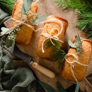 Three orange cakes on cutting board wrapped with greenery.