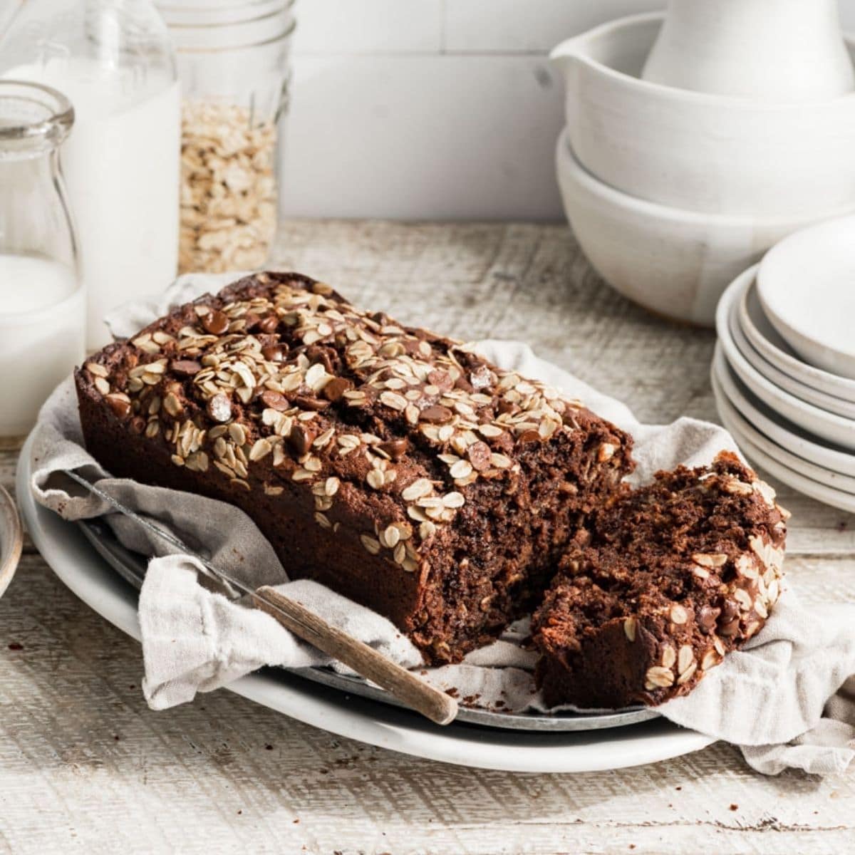 Loaf of chocolate banana bread sliced on an oval plate next to white plates.