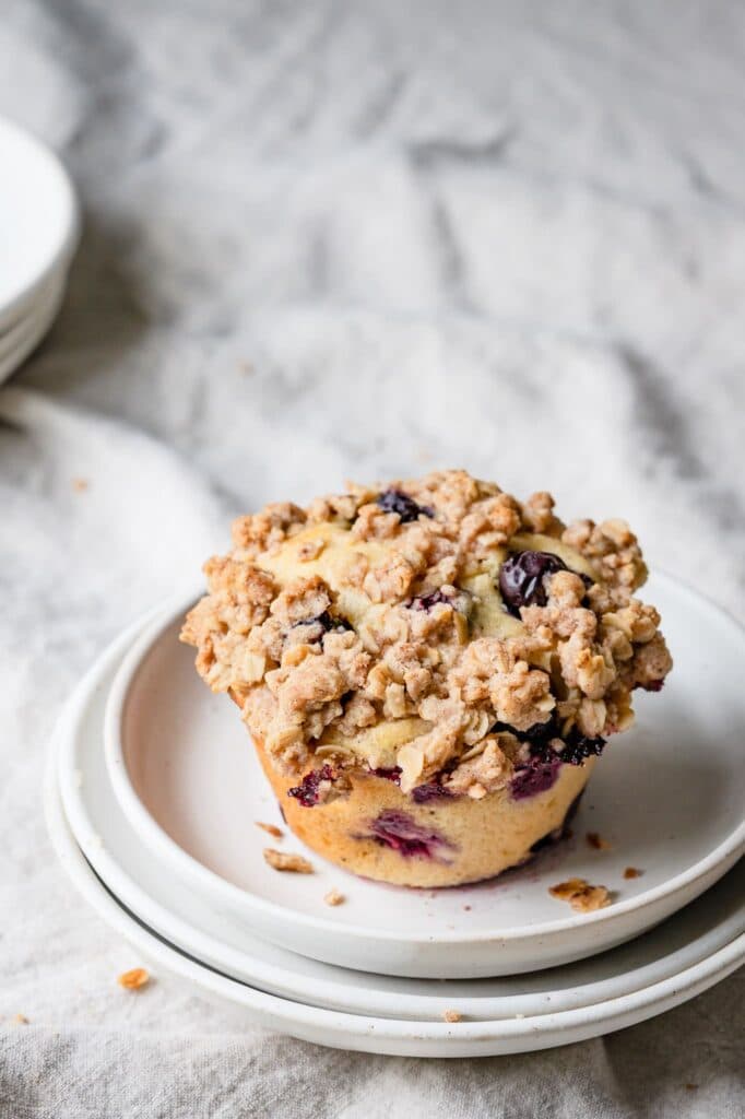 Blueberry muffin on stack of white plates.