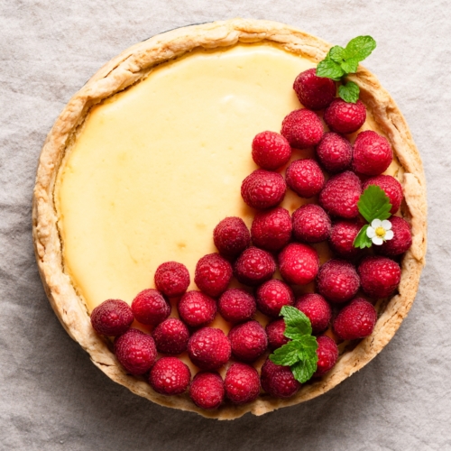 Overhead view of a lemon cheesecake topped with fresh raspberries inside a pie crust.