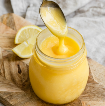 Jar of lemon curd with a spoon dripping some of the curd back into the jar.