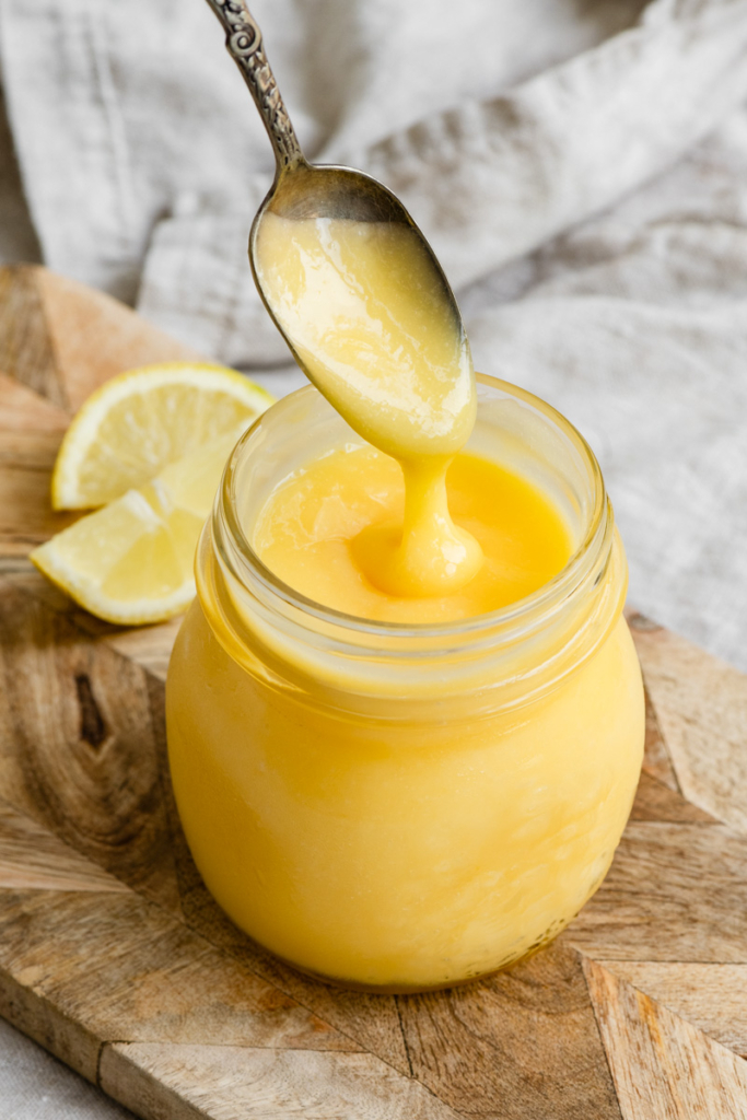 Jar of lemon curd with a spoon dripping some of the curd back into the jar.