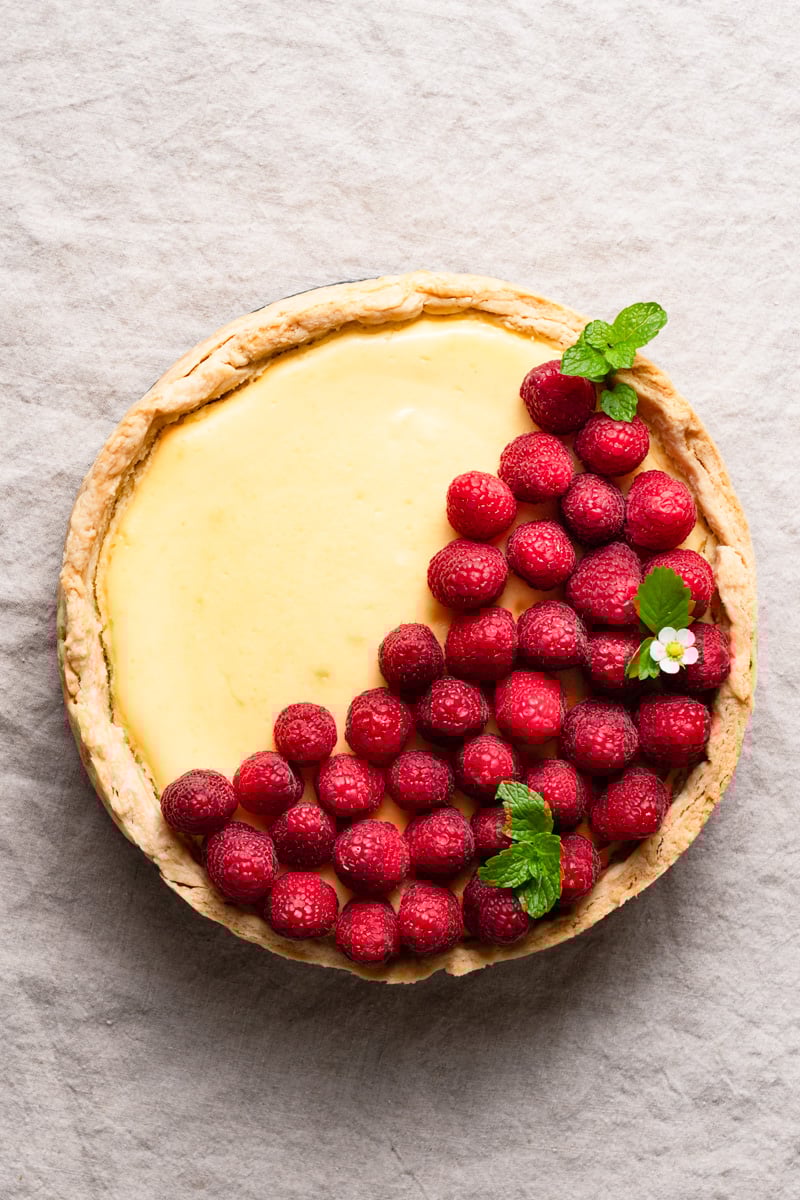 Overhead view of a lemon cheesecake topped with fresh raspberries inside a pie crust.