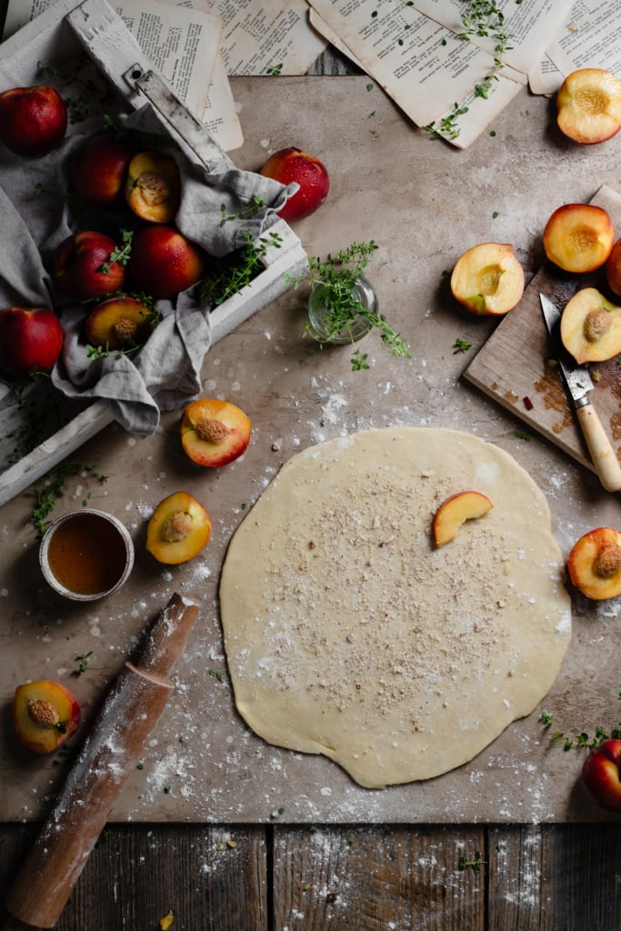 Pie dough rolled out in a circle topped with almond flour and surrounded by peaches.