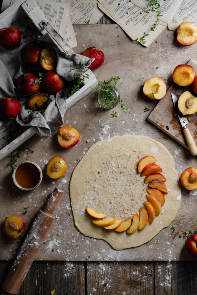 Pie dough on a table with sliced peaches in a half circle on the top.