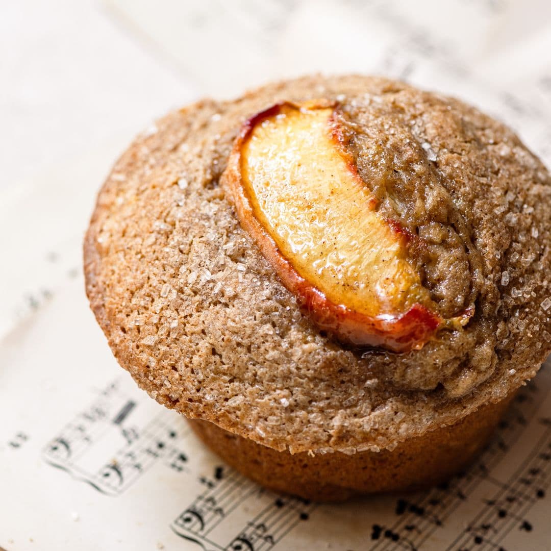 Close up of a baked muffin topped with a peach slices on a sheet of music.