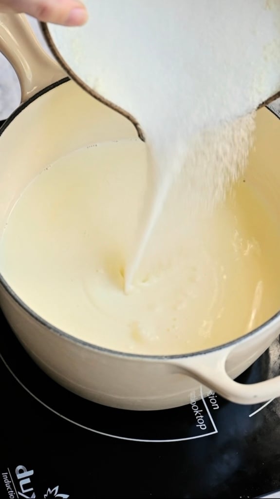 Sugar being poured into a saucepan full of cream.