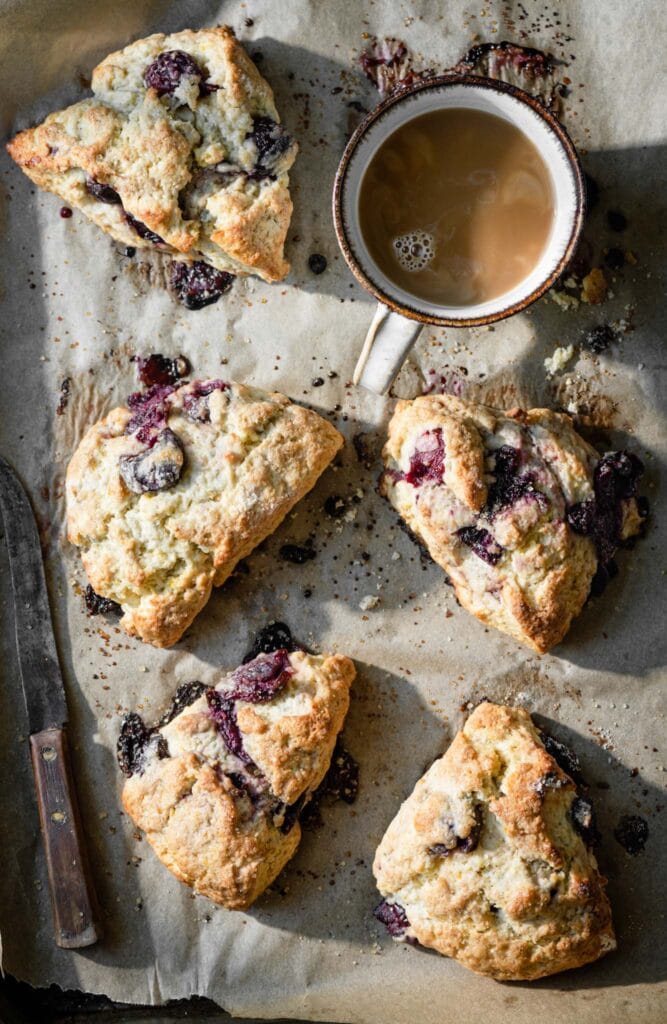 Baking tray with five cherry scones and a cup of coffee.