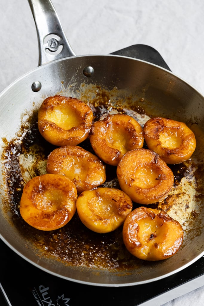Yellow peach halves, face up in skillet of melted butter and brown sugar.