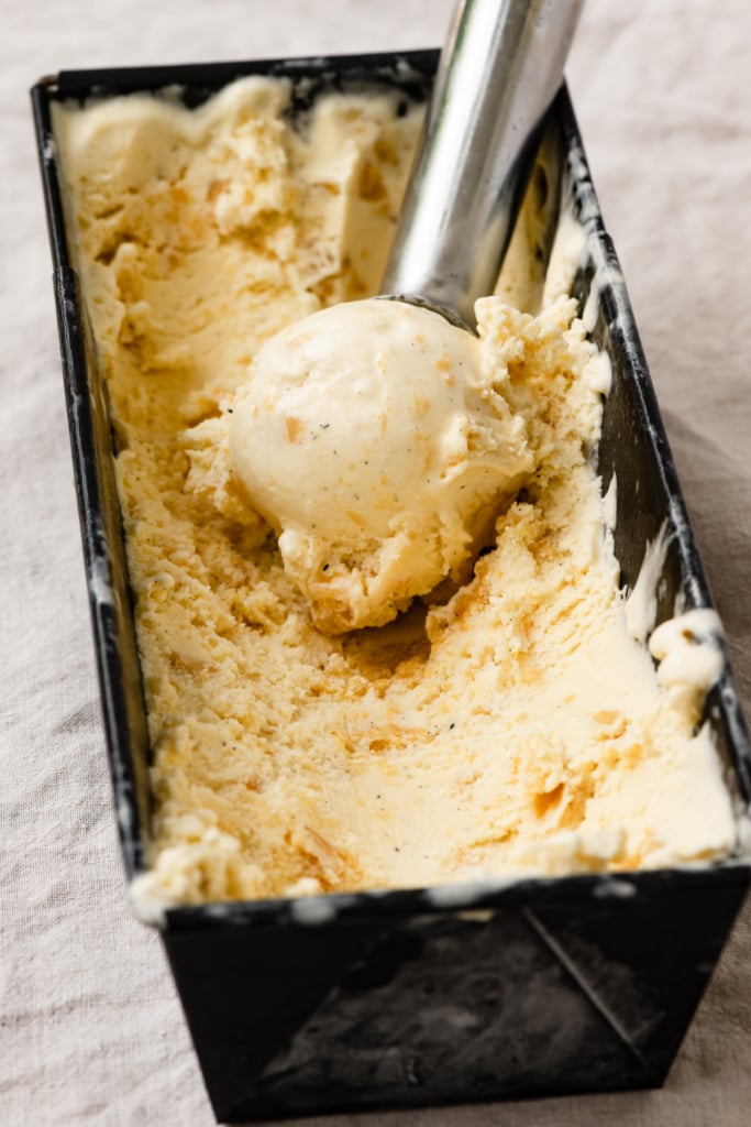 Ice cream scoop with a scoop of ice cream sitting inside a container full of peach ice cream.