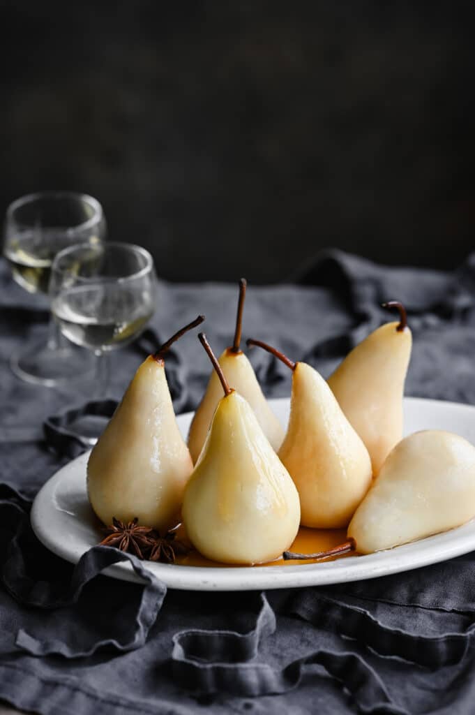 White wine poached pears on table with two glasses of wine.