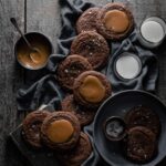 chocolate cookies topped with caramel and sea salt on wood table.