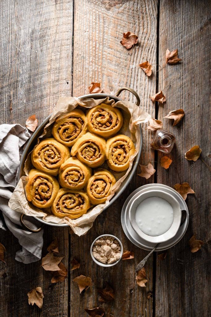 Tray of baked pumpkin cinnamon rolls on wooden table.