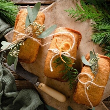 Mini orange cakes tied with string and greenery on a cutting board.