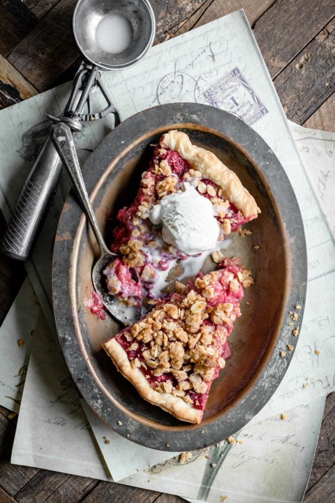 Two slices of raspberry pie in a metal dish topped with melted vanilla ice cream.