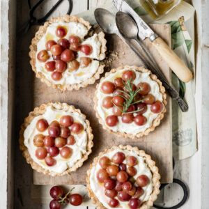 Four mini mascarpone tarts topped with red grapes in a wooden box.