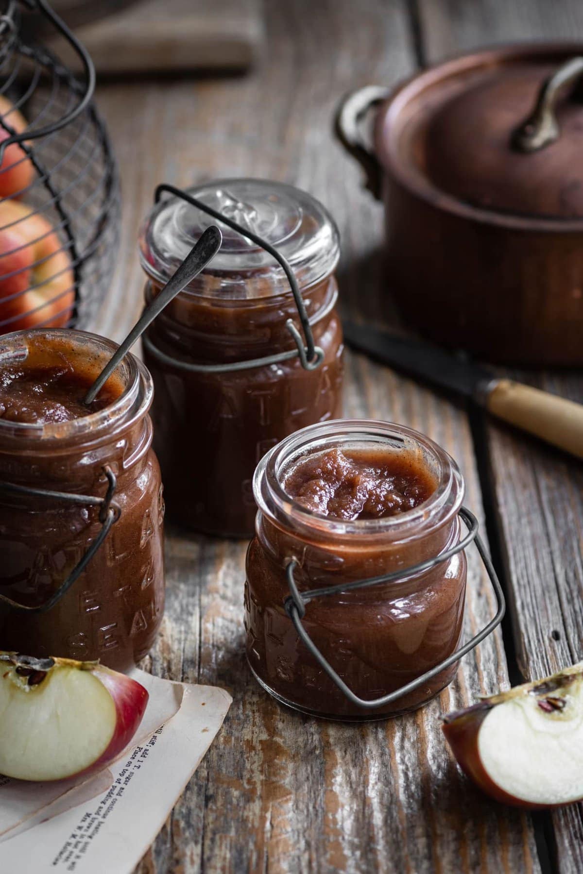 Jars filled with apple butter on wooden table with maple syrup.