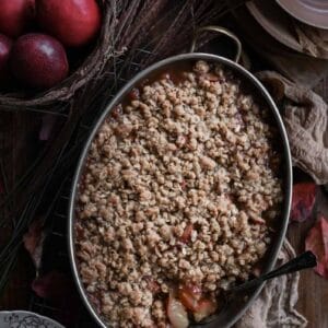 Baked fruit crisp on wood table with a serving spoon scooping out the filling.