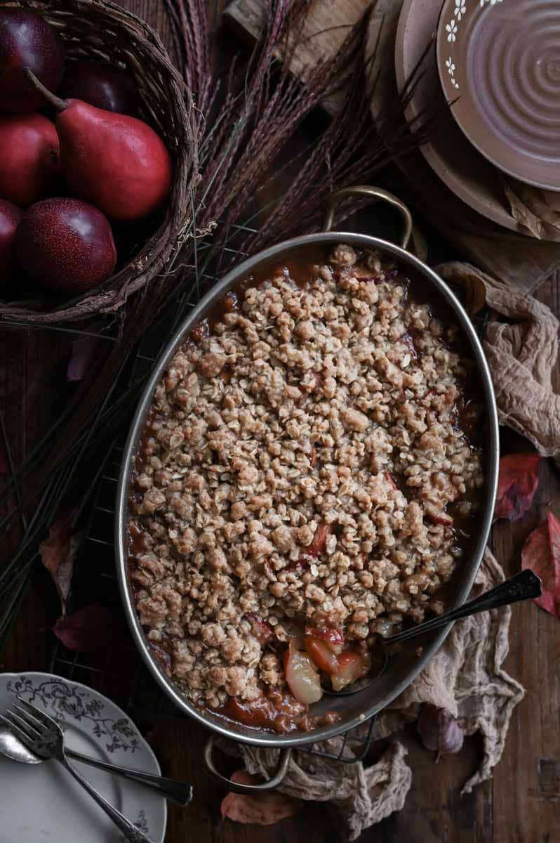 Baked fruit crisp on wood table with a serving spoon scooping out the filling.