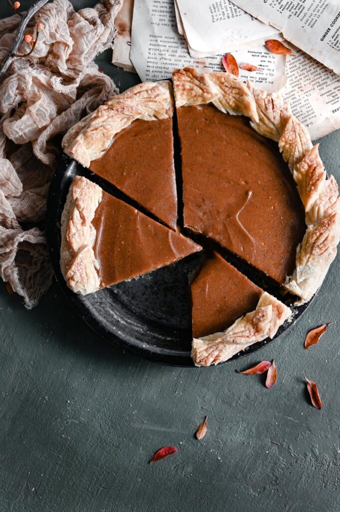 Sweet potato pie with leaf design crust in pan with slices cut.
