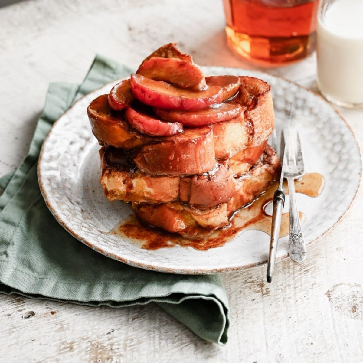 Stack of french toast with cooked apples covered in syrup on a plate.
