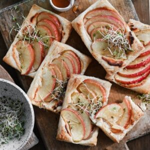 Apple tarts made with puff pastry topped with microgreens on a wooden cutting board.