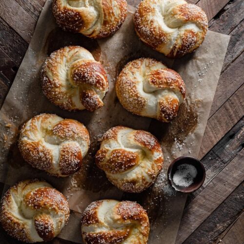 Eight pretzel knots placed in a row on parchment paper sheets.