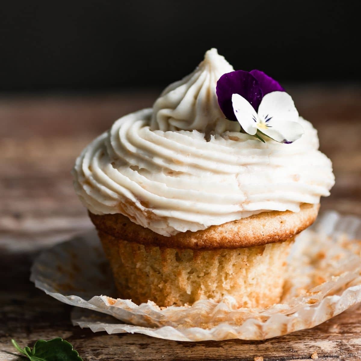 Single frosted vanilla cupcake on a wood table.