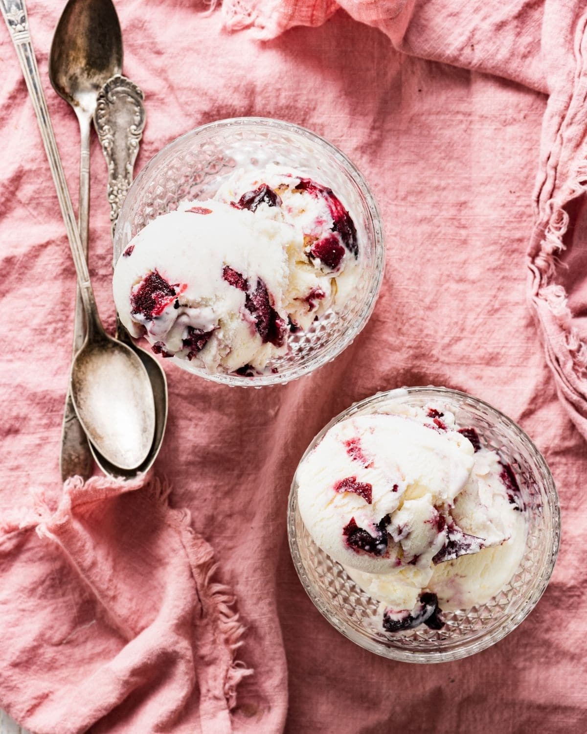 Two glass goblets filled with cherry chunk ice cream next to silver spoons.