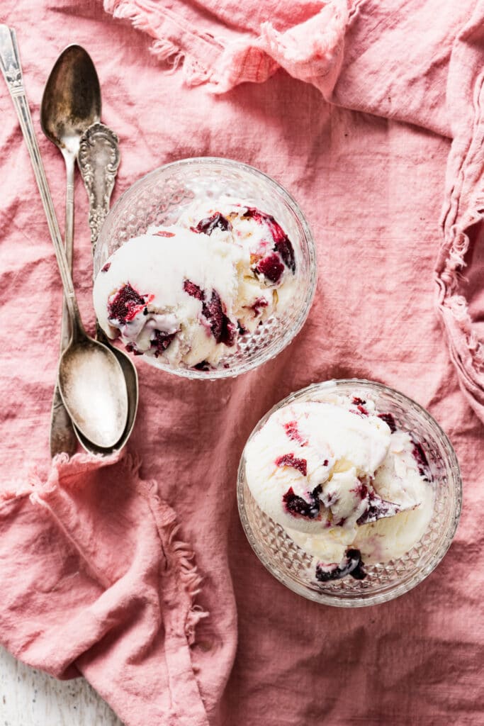 Two glass goblets filled with cherry ice cream placed on a pink linen.