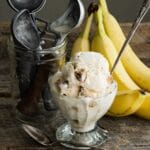Closeup of a glass goblet filled with banana ice cream and a spoon next to bananas.