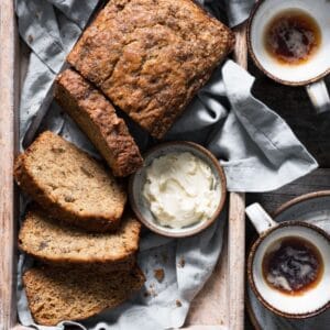 Sliced loaf of banana bread with butter and coffee on breakfast tray.