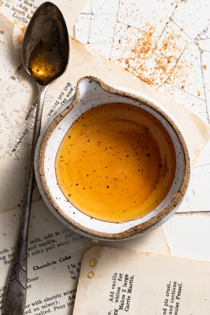 Small bowl filled with maple syrup next to a spoon on recipe cards.