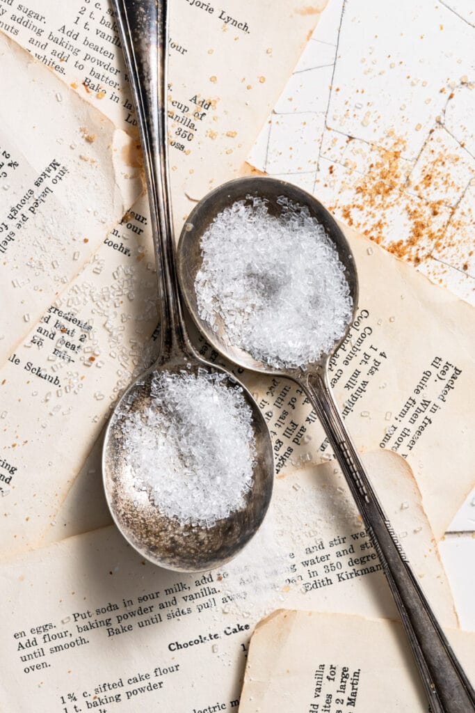 Two metal spoons filled with sparkling sugar on recipe cards.