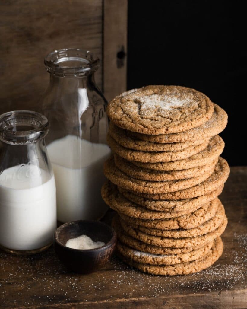 Stack of thin cookies next to a jar of milk on wood box.