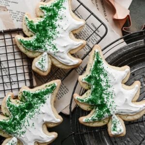 Frosted sugar cookie sin the shape of trees on cooling racks.