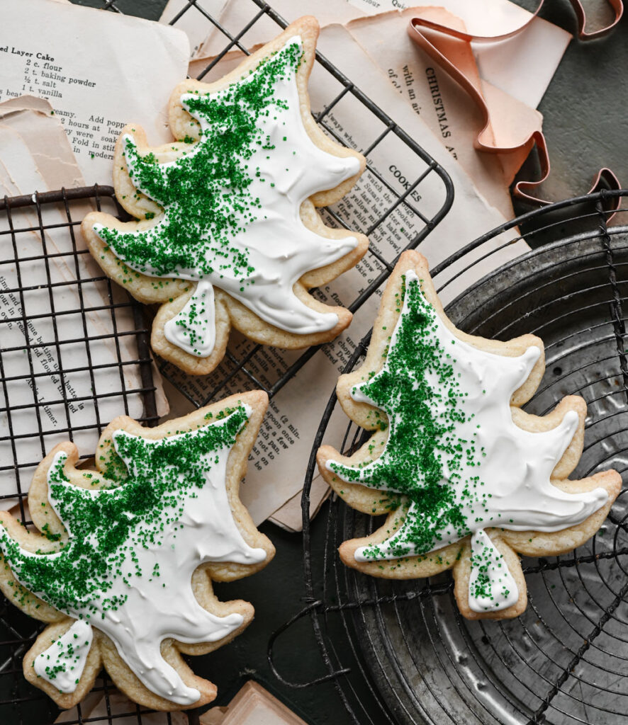 Three green and white decorated tree shaped  sugar cookies on wire rack.