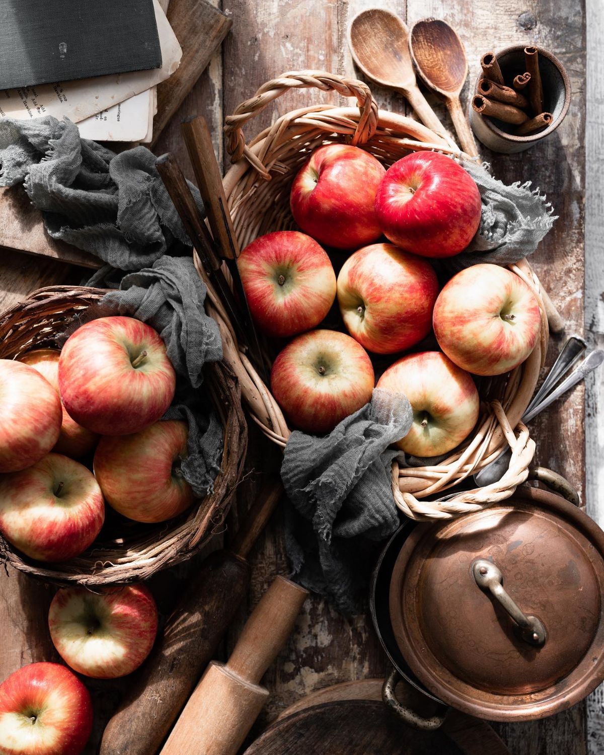 Basket of apple on wood table next to baking tools.