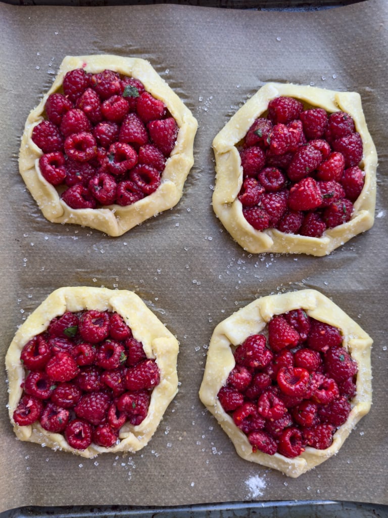 Overhead view of four unbaked raspberry filled pies on a baking sheet.
