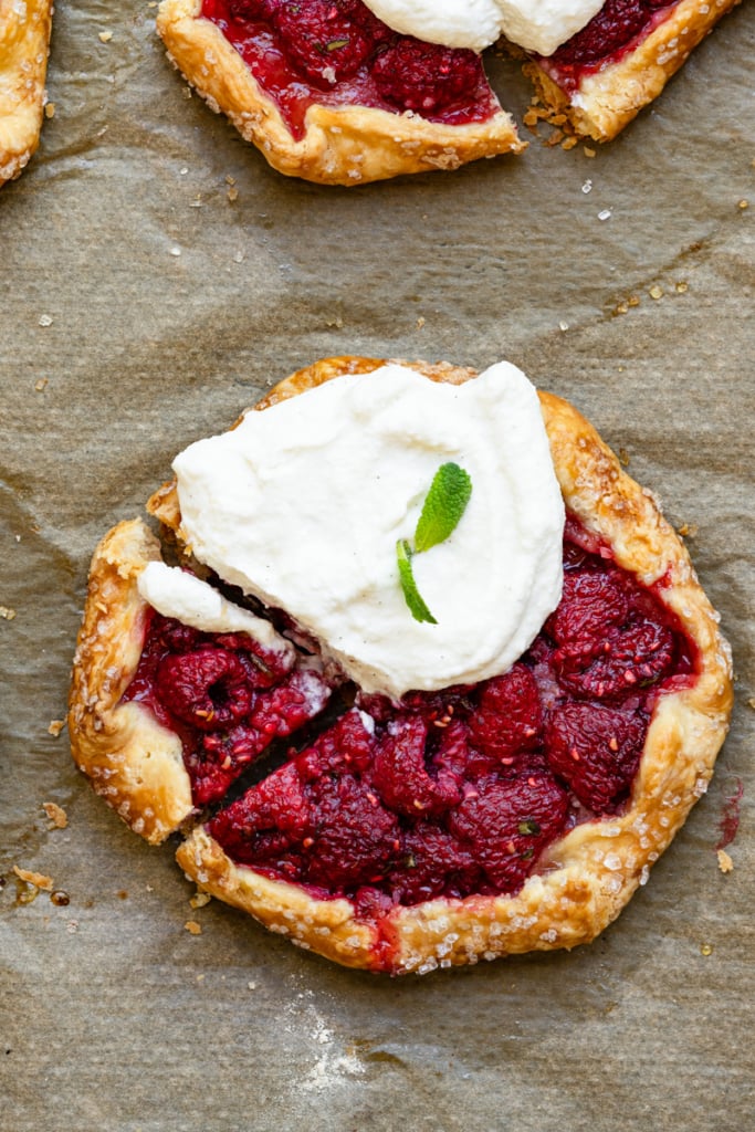 Overhead view of a hand shaped raspberry filled tart topped with cream on a baking sheet.
