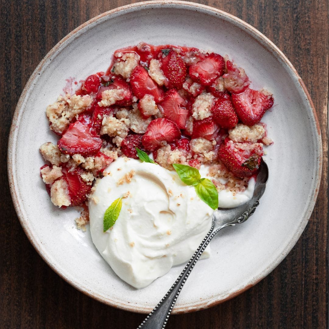 Bowl filled with cream and roasted strawberries.