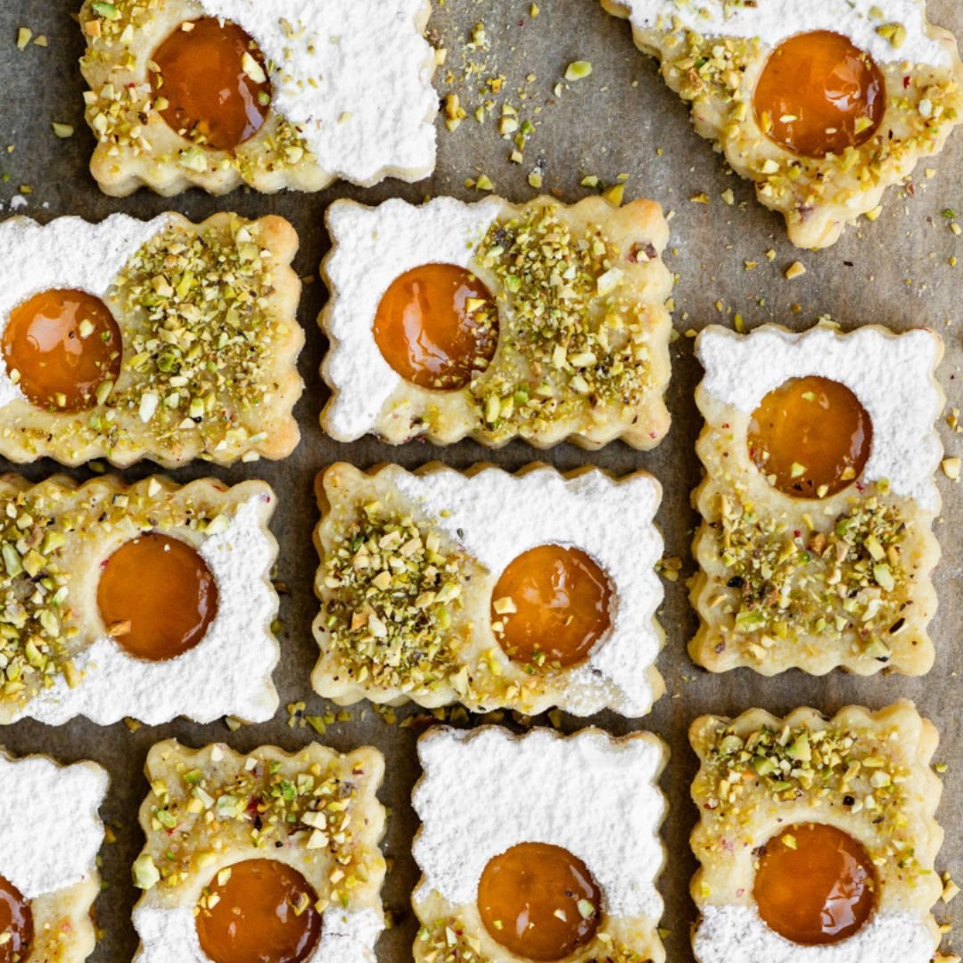 Rectangular linzer cookies topped with powdered sugar and pistachios placed on parchment paper.
