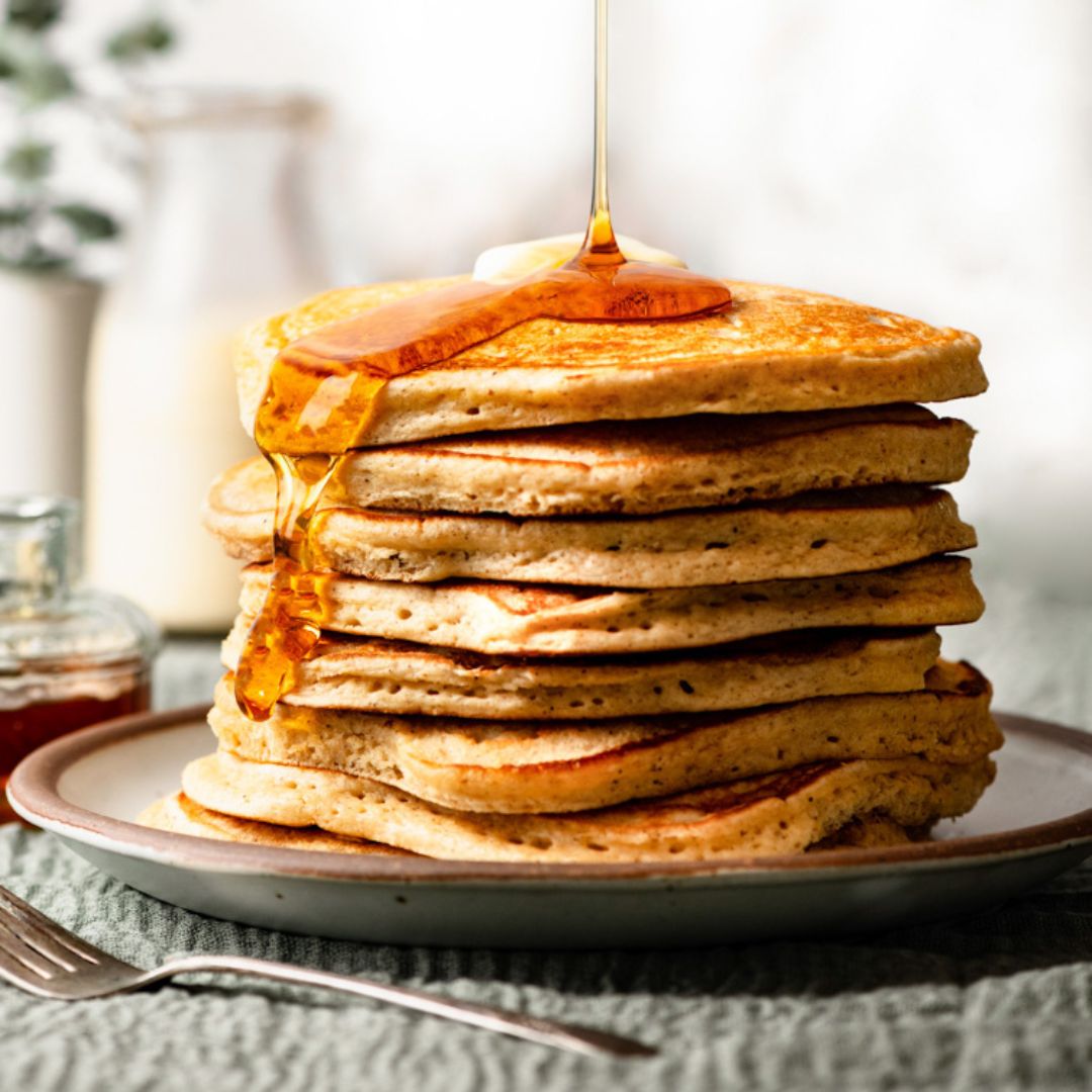 Stack of eggnog pancakes on a plate, topped with butter and maple syrup.