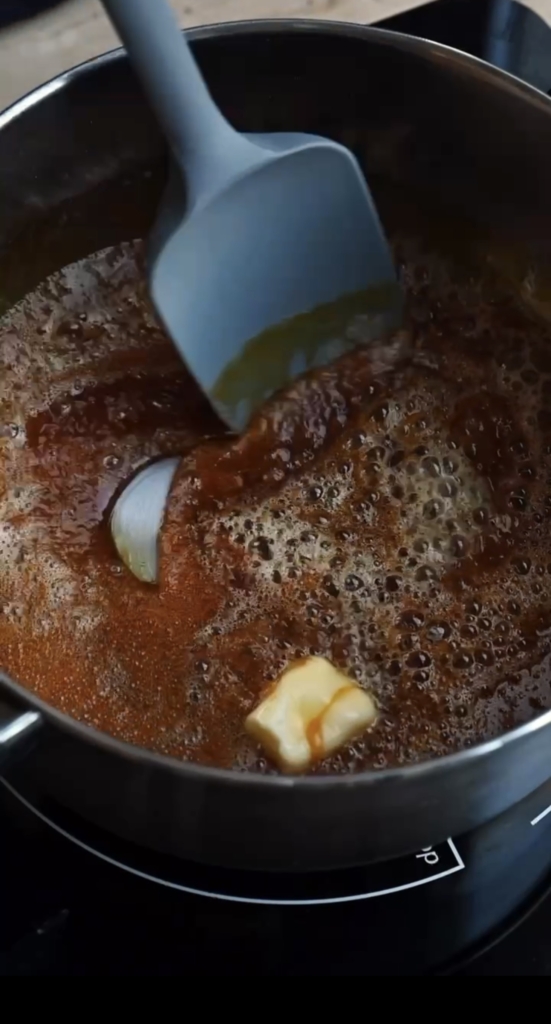 Pot of hot caramel with a spatula stirring in chunks of butter.