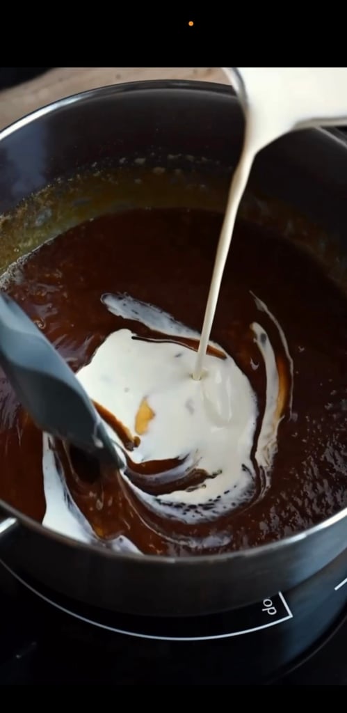 A pot of caramel with cream being poured in from above.