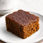Slice of gingerbread cake on a plate next to a cup of coffee.